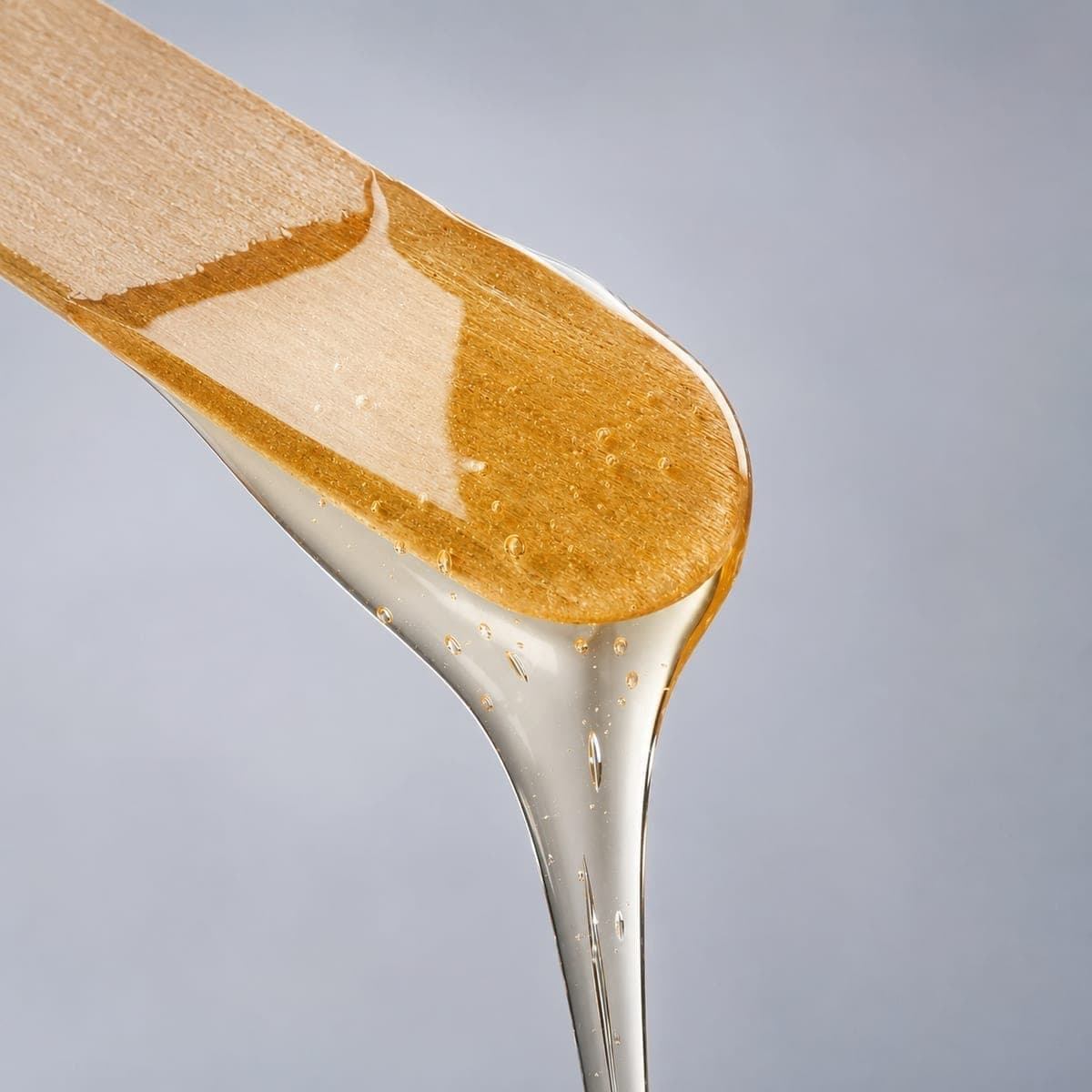 Spatola in legno da cui cola cera densa e trasparente per l'epilazione